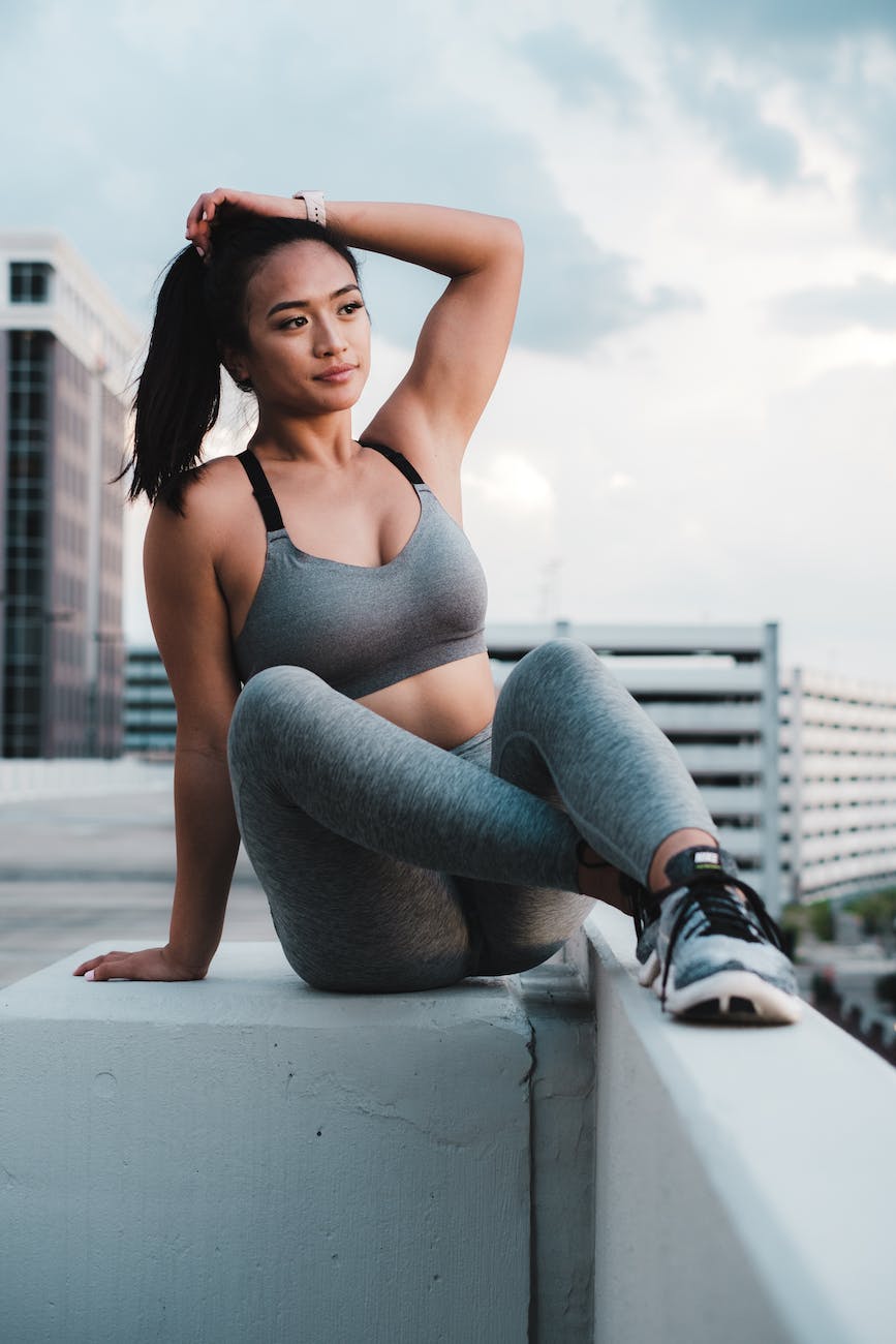 a woman in gray leggings and sports bra sitting with her hand on her head