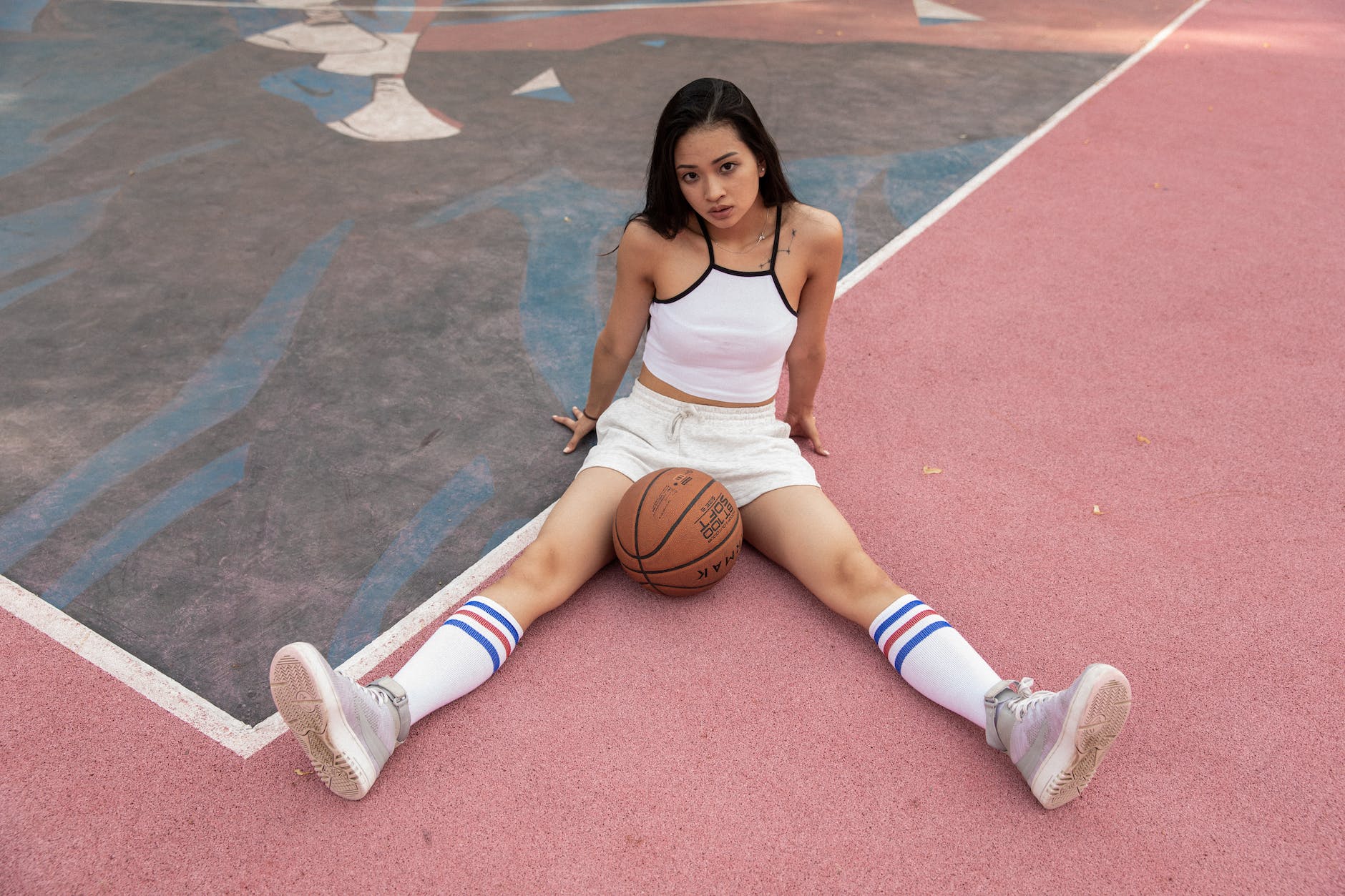 attractive asian woman sitting with basketball ball on court