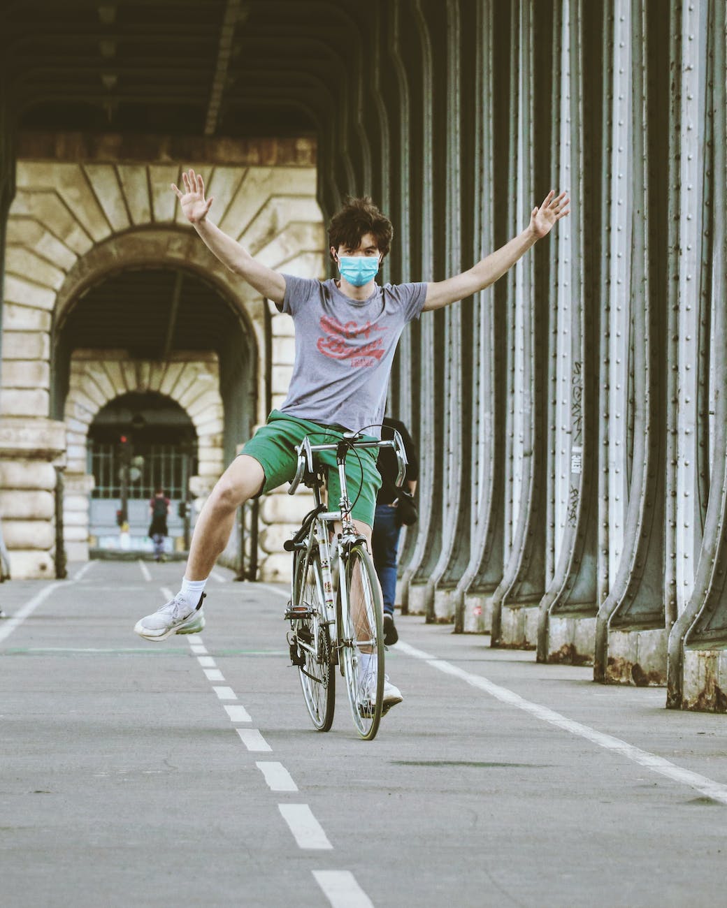 anonymous sporty man riding bike on city promenade with outstretched arms